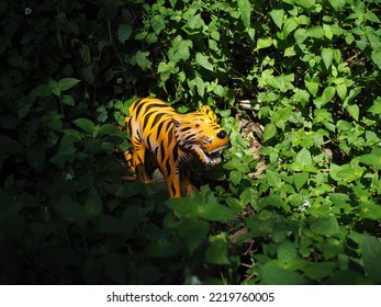 Bight Sunshine On Ceramic Tiger Hidden In Lush Green Jungle Leaves With Dark Shafow Behind 