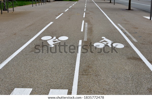 Bike lanes or cycle paths in\
opposite directions along the car road in the city of Belfort in\
France. The biking symbols and the lines are painted in white\
color.