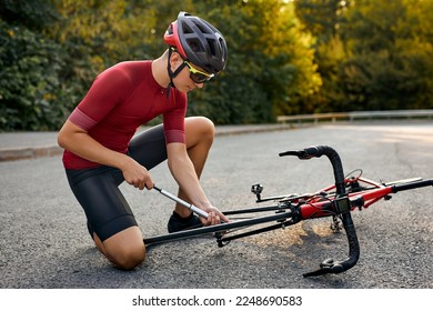 bike maintenance. sportsman is pumping up tyre. outdoors at daytime. young caucasian guy in sportive outfit is going to ride a bike. Inflating the tire of bicycle. Cyclist repairs bike on road. - Powered by Shutterstock