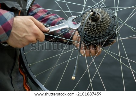 The bike mechanic installs a new cassette on the motor wheel. Repair of electric bicycles. Mechanic's hand and wrench close-up. Replacement of worn-out equipment on a mountain bike
