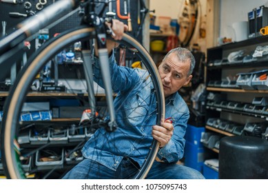 Bike mechanic repairing a wheel. Mechanic or serviceman installing wheel on a bicycle in workshop. Mature man working in a biking repair shop - Powered by Shutterstock