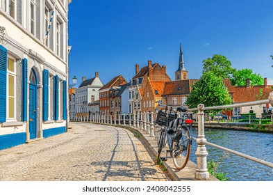 Bike near metal fence, embankment street of Sint Annarei water canal, buildings in Brugge old town, Bruges city historic center in sunny day, Saint Anna Church spire, West Flanders province, Belgium - Powered by Shutterstock