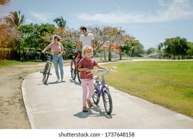 Bike Ride. Family Walks In The Park On A Sunny Day. There Are Seven Face Masks Of Different Colors On The Faces, Against The Coronavirus Covid-19