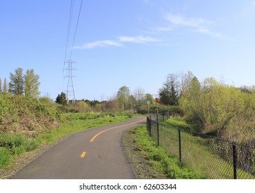 A bike route and walking path made of black asphalt is seen close up in a wooded setting that is part of power line park in Beaverton, Oregon.