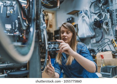 Bike Service: Mechanic Servicewoman Repairman Installing Assembling Or Adjusting Bicycle Gear On Wheel In Workshop. Young Woman Working In A Biking Repair Shop