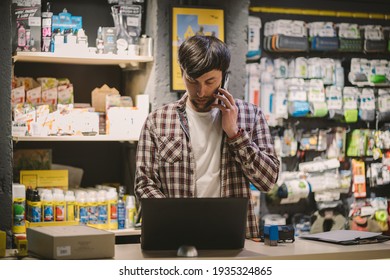 Bike Shop Owner At Work. Store Employee Takes An Order By Mobile Phone At Table Near Laptop In Travel And Sporting Goods Store. Small Business, Communication, People And Service Concept.