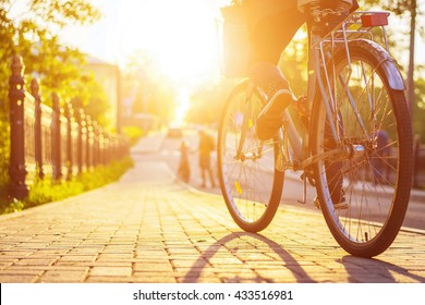 Bike at the summer sunset on the tiled road in the city park. Cycle closeup wheel on blurred summer background. Cycling down the street to work at summer sunset. Bicycle and ecology lifestyle concept. - Shutterstock ID 433516981