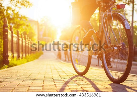 Bike at the summer sunset on the tiled road in the city park. Cycle closeup wheel on blurred summer background. Cycling down the street to work at summer sunset. Bicycle and ecology lifestyle concept.