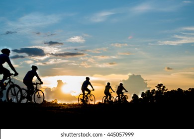 Bike Team Ride In The Evening With The Orange Sky,Silhouette Background.