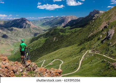 Bike tour. A man with a bicycle on the pass on the background of a magnificent valley with a sirpantine road going down. Teskeytorpo Pass. Kyrgyzstan - Powered by Shutterstock