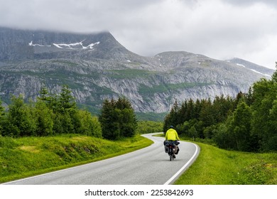 Bike travel tourist rides on an empty road in northern Norway surrounded by forest and high mountains - Powered by Shutterstock