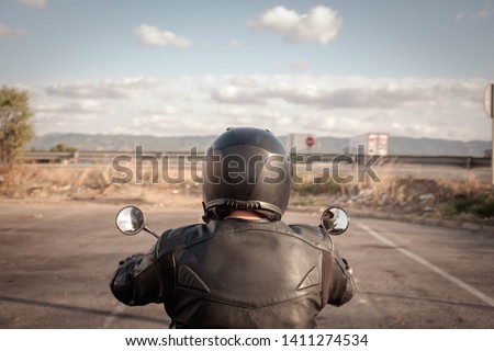 Biker in black leather jacket and black helmet, back view