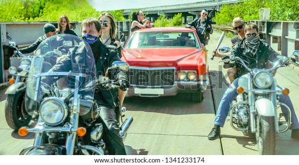 Biker Couple with motorcycle Chopper style Man and\
woman ride with high speed.girl wear leather jacket and sunglasses\
against park background Gang of groups of armed people. baseball\
bat in hand