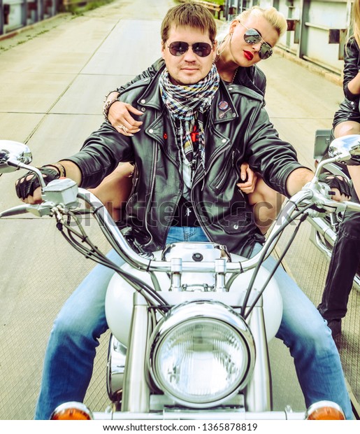 Biker Couple
with motorcycle Chopper style Man and woman ride with high
speed.girl wear leather jacket and sunglasses against city
background. Gang of groups of armed people.
