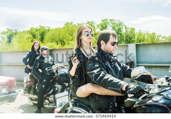 Biker Couple with motorcycle Chopper style Man and\
woman ride with high speed Cute girl wear black leather jacket and\
stylish sunglasses against urban background Gang of groups of armed\
people