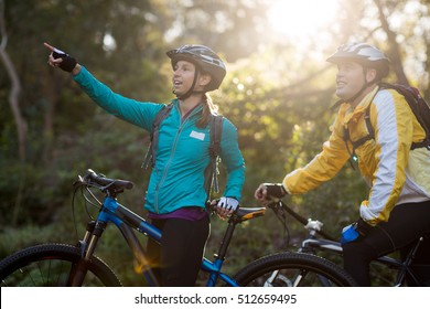 Biker couple with mountain bike pointing in distance at countryside