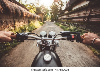 Biker Driving His Motorcycle On Country Road In A Village. Point Of View With Focus Is On The Handlebar And Man Hands.