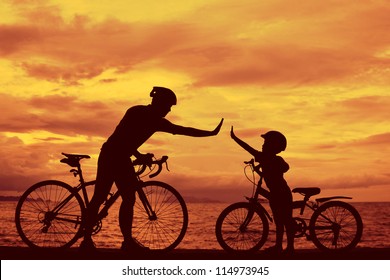 Biker family silhouette , daddy and son at the beach at sunset.