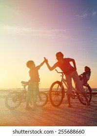 Biker Family Silhouette At Sunset, Mother With Two Kids On Bikes