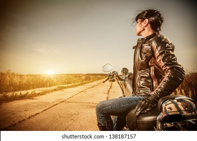 Biker Girl In A Leather Jacket On A Motorcycle Looking At The Sunset.