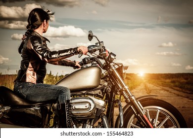 Biker Girl In A Leather Jacket On A Motorcycle Looking At The Sunset.