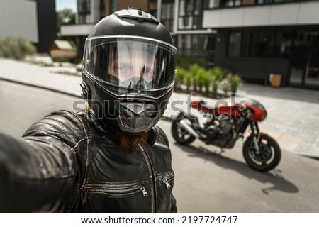 Biker in helmet takes a selfie in front of motorcycle