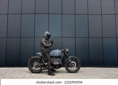 Biker man with Black blue rebuilt vintage custom motorcycle cafe racer in front of wall - Powered by Shutterstock