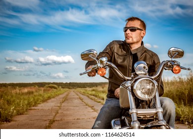 Biker Man Wearing A Leather Jacket And Sunglasses Sitting On His Motorcycle