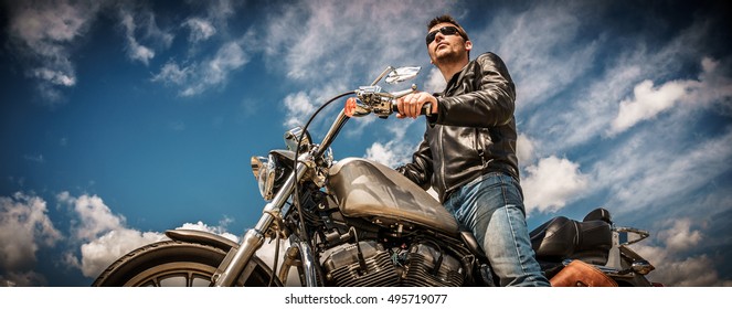 Biker Man Wearing A Leather Jacket And Sunglasses Sitting On His Motorcycle.