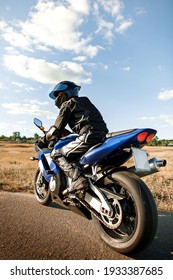 Biker oder Motorradfahrer in schwarzem Lederanzug und Helm sitzt auf einem sportlichen Motorrad und blickt in die Ferne. Vertikale Fotoausrichtung
