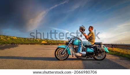 Biker on a classic motorcycle holding a black helmet at sunset