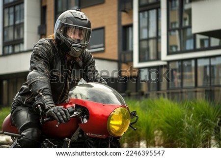 Biker in protective clothing rides a motorcycle in front of the house