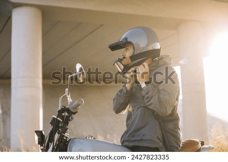 A biker puts on a helmet while sitting on a motorcycle.A man rides a motorcycle at sunset.
