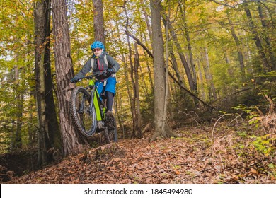 Biker riding downhill with a modern electric bicycle or mountain bike in autumn or winter setting in a forest. Modern e-cyclist in woods.