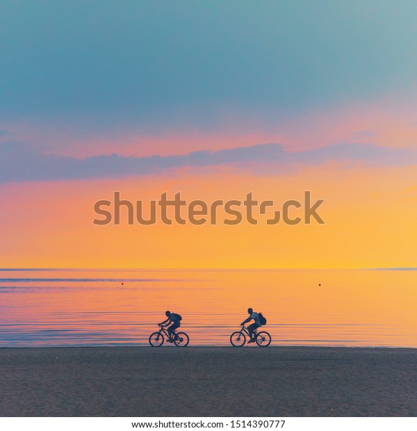 Biker silhouette riding along dune beach at calm\
cloud sunset view on mtb bike Sporty company group of friends on\
bicycle outdoors, cyclist mountain biking city park path concept.\
dad son fit exercise