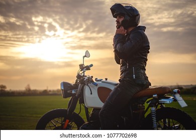 Biker sitting on motorcycle and putting on his helmet while sunset is in the background
