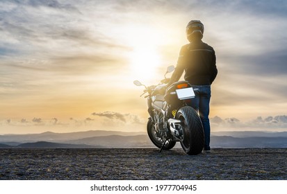 biker standing next to the motorcycle, watching the sunset - copy space
				