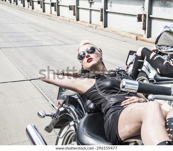 Biker Woman on\
motorcycle against metal bridge background Young brutal cute girl\
lie on chopper and wear black leather dress and stylish sunglasses \
Empty space for inscription\
