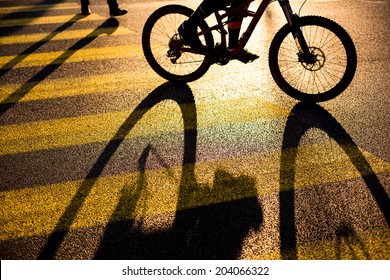 Biker/Cyclist On A Crossing In A City Casting A Long Shadow