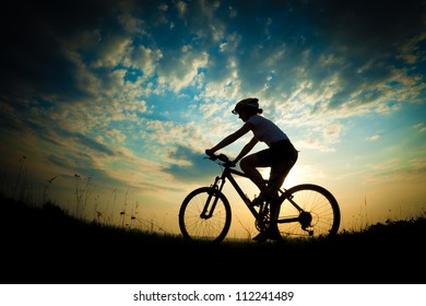 Biker-girl at the sunset on the meadow