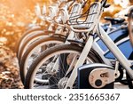 Bikes or Electric Bicycles Charging Battery in Public Parking lot in Autumn. Bike Sharing System. Modern Blue e Bikes with Basket for Rental Service. Eco Transport in Green City