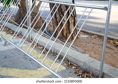 A Bikes Stand Made Of Stainless Steel For Parking In A Public Parking Spot. Sportsmen And Active People Also Need Their Own Parking Spot. In The Background You Can See Trees And A Parking Spot Fo