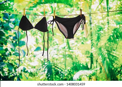 Bikini hanging on clothes line outside on balcony. Summer vacation icon - woman clothing fashion black swimwear eco friendly laundry with green background.