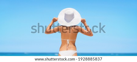 Bikini model on beach view from behind wearing hat as sun protection on summer vacation. Travel panoramic banner woman fit back. Wellness skincare body care concept.