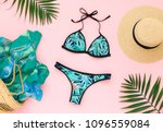 Bikini swimsuit with tropical print, straw hat, wicker beach bag, sarong and tropical date palm leaves on pink background. Overhead view of woman
