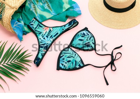 Bikini swimsuit with tropical print, straw hat, wicker beach bag, sarong and tropical date palm leaves on pink background. Overhead view of woman's swimwear and beach accessories. Flat lay, top view.