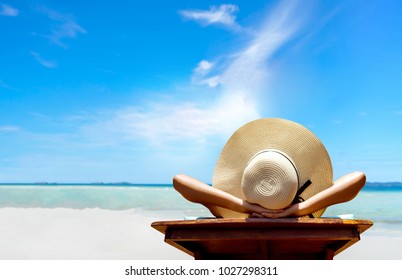 Bikini woman sexy in relax beach and resting resort in vacation on summer season with sunhat sitting chair sunbath with swimsuit alone at island lifestyle on weekend holidays