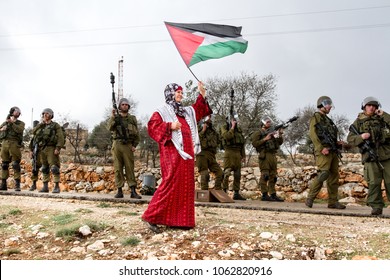 Bilin, Palestine, December 31, 2010: Palestinian woman walks with Palestinian flag in front of Israel Defence Force soldiers during weekly demonstrations against Palestinian land confiscation in Bilin