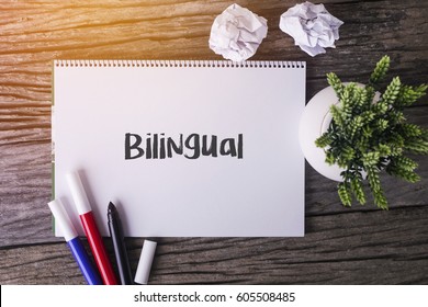 Bilingual Word With Notepad And Green Plant On Wooden Background