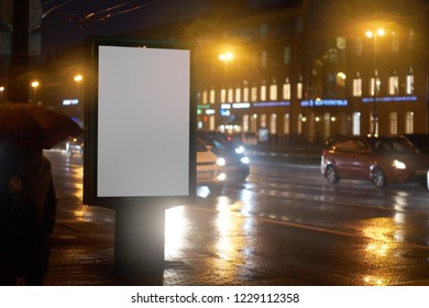 The Billboard Ad CityLight, Shines In The Night City. Mockup With A White Field For Advertising. Rainy Evening, Wet Weather And Road